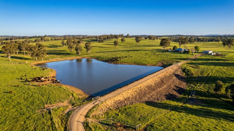 Scenic view of Big Ditch water reservoir with surrounding green fields and clear blue sky.