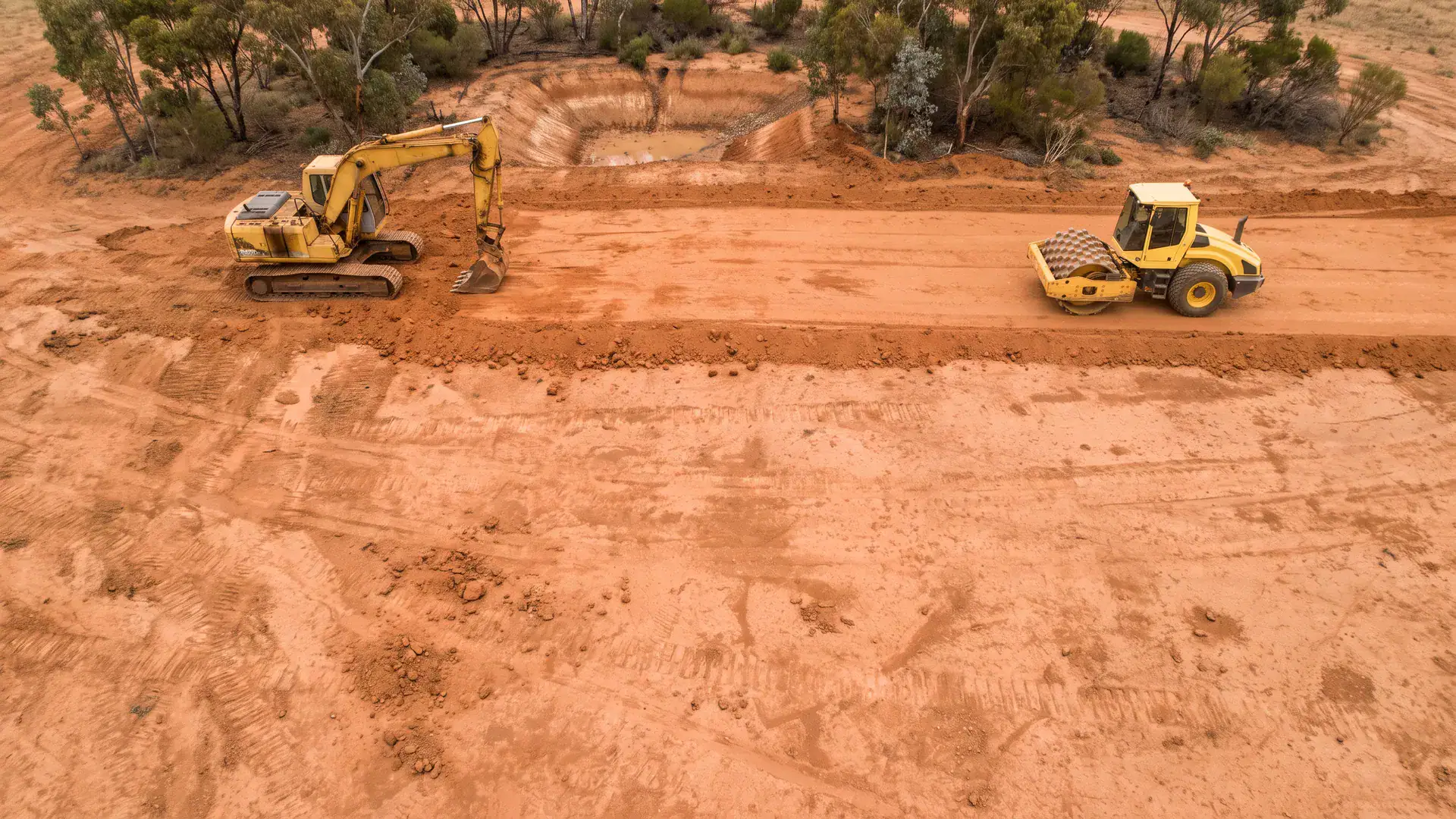 Excavator and padfoot roller on an Australian site, showing complementary farm dam building equipment