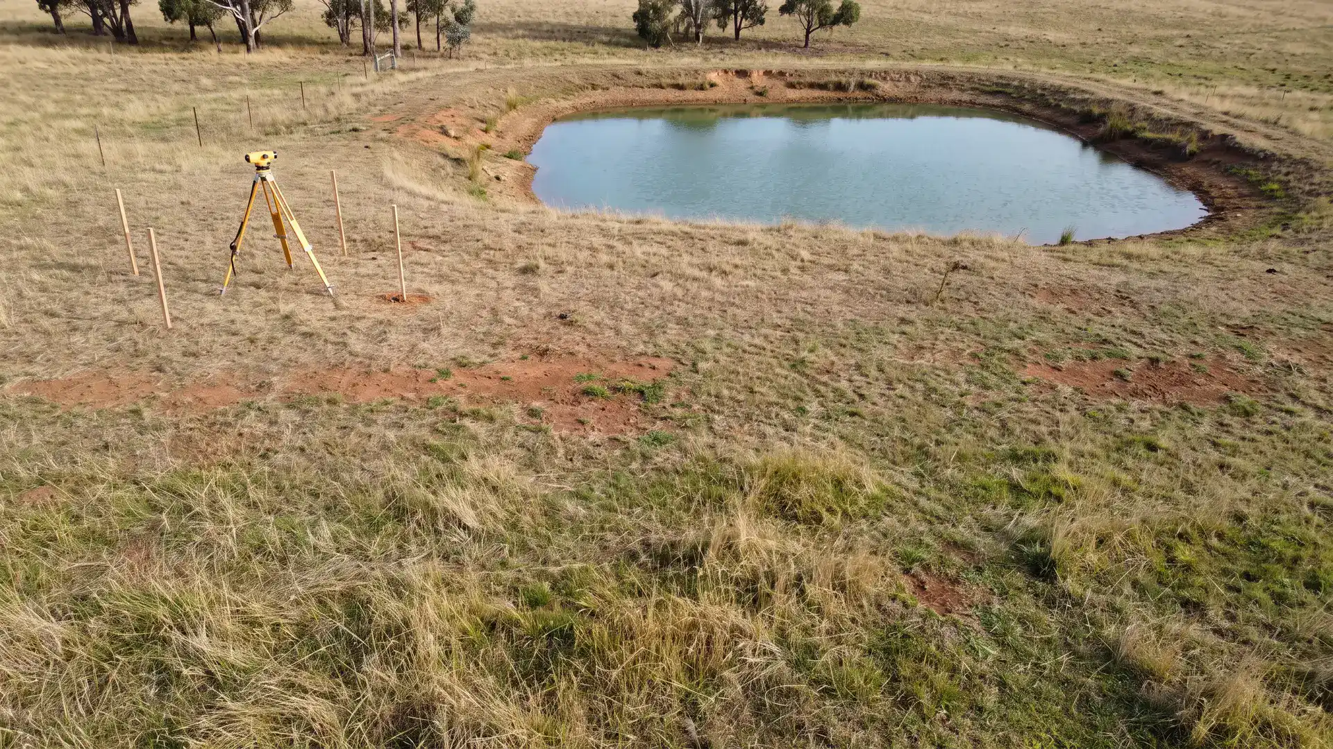 Survey tripod beside a rural dam for farm dam permit Victoria site planning