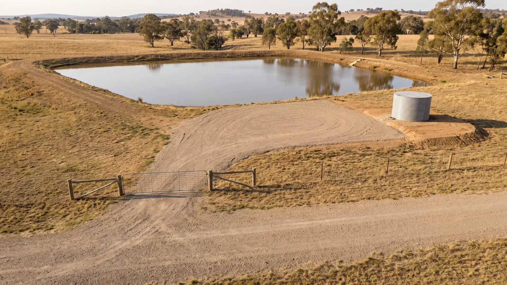 Farm dam bushfire water supply with a gravel access area and water tank in an Australian paddock