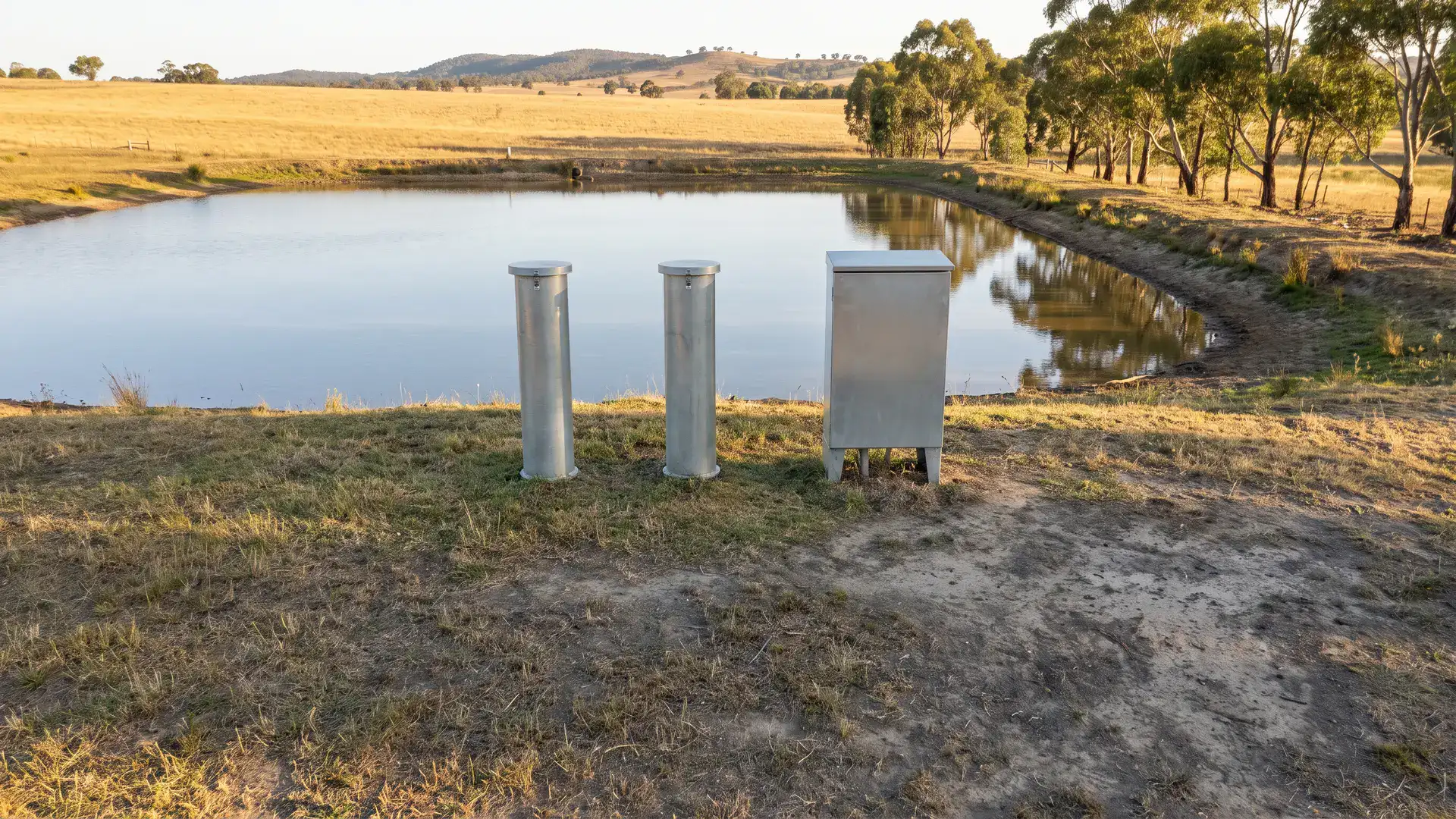 Dam wall monitoring instruments with capped piezometer casings beside an Australian farm dam