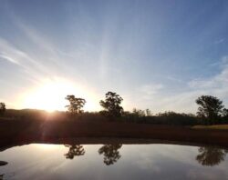 Dam construction at sunset with water reflection in rural landscape.