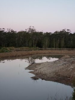 Heavy dam construction site by Big Ditch Dam Building Company by a water body at dusk.