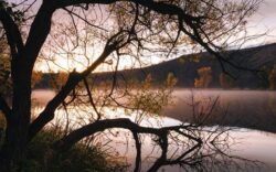 Dam construction site at sunrise with water and trees, Big Ditch Dam Building Company expertise.
