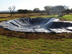 Lined pond liner for dam construction on rural land for water storage and irrigation.