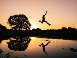 1. Silhouette of a person jumping by water at sunset, nature, outdoor activity, carefree lifestyle.