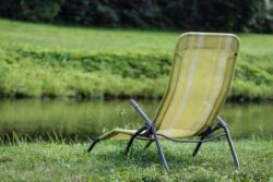 Relaxing outdoor chair by water with lush greenery in background.